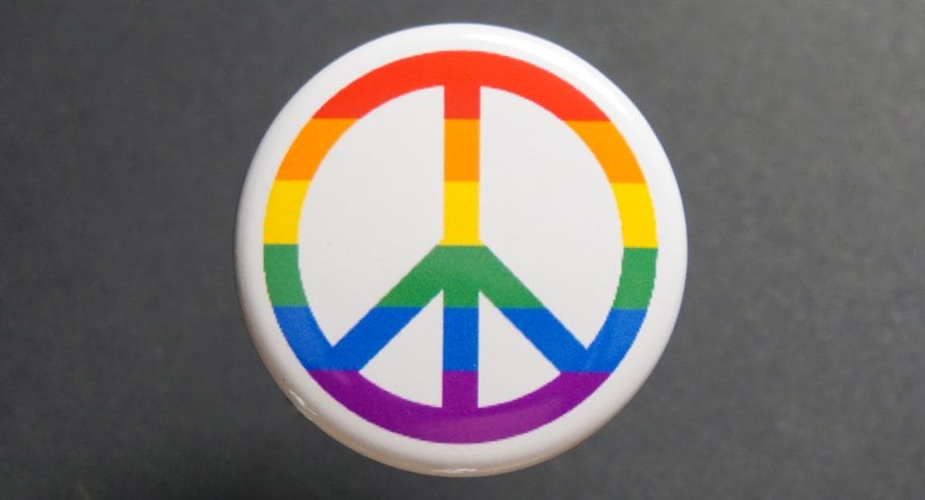 Badge militant combinant le drapeau lgbt avec le signe paix