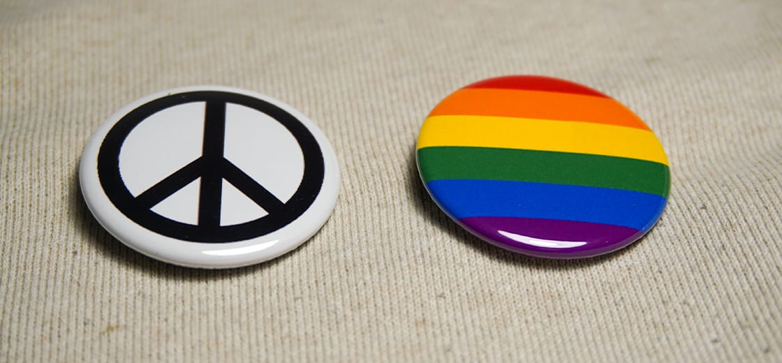 Quelqu'un portant des badges Badge·Ta·Mère sur sa veste, avec plusieurs badges militants épinglés sur un blouson